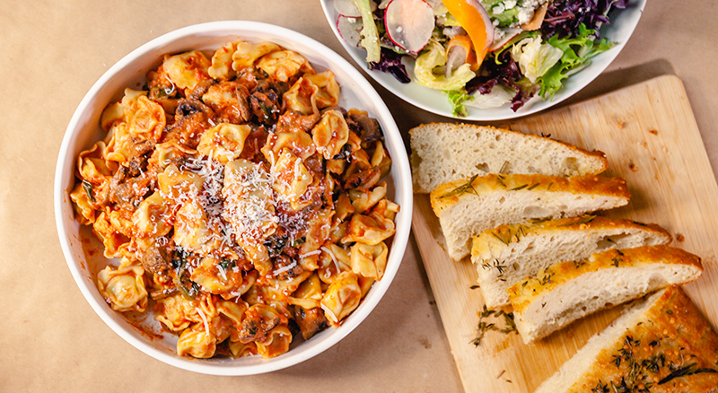 Dish of black radish pasta, bread on cutting board, and bowl of salad